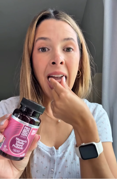 Woman holding a bottle of Probiotic Women's Health supplement near her mouth.