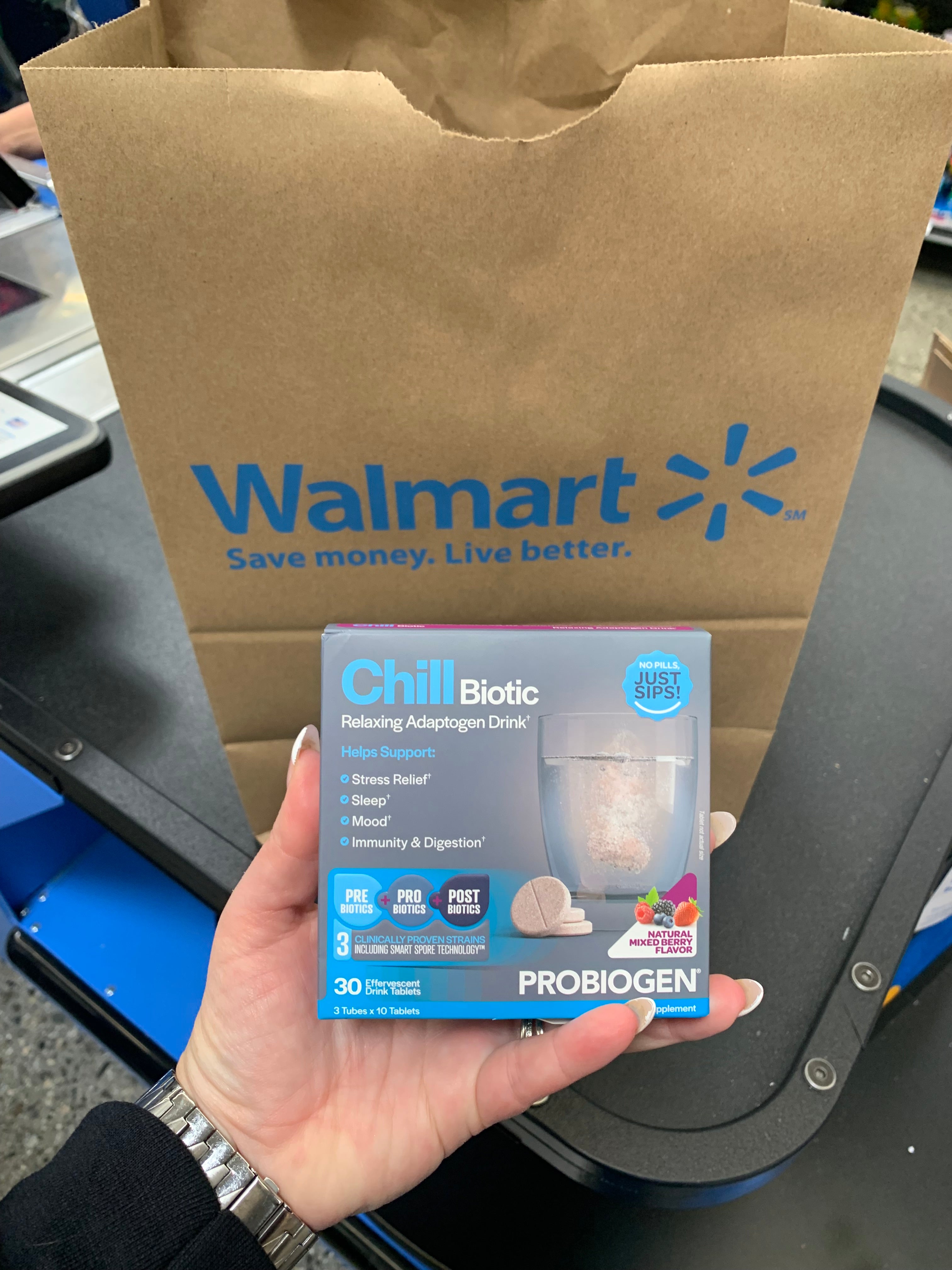 Hand holding a package of Probiotic supplement in front of a Walmart shopping bag.