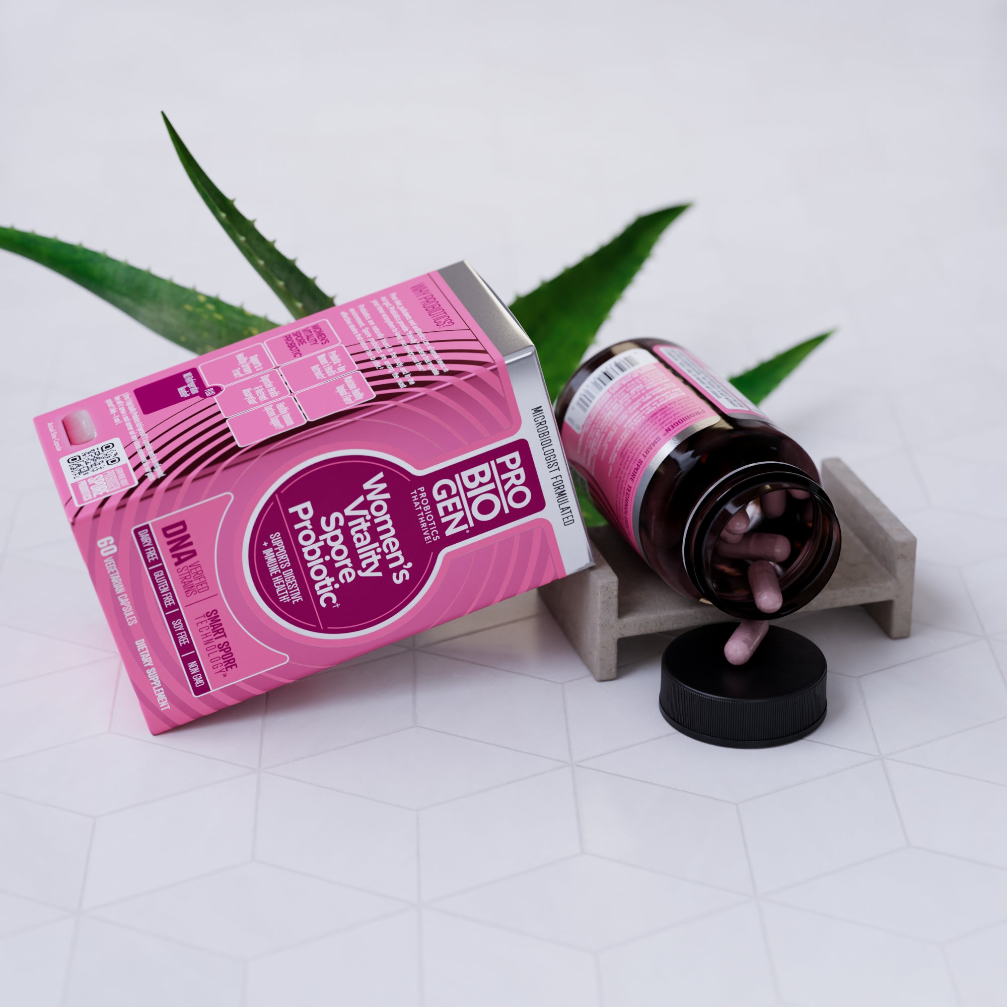 Pink women's Vitality Spore probiotic packaging with aloe vera leaves on a white surface.